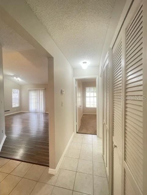 hall with lofted ceiling, light tile patterned floors, and a textured ceiling