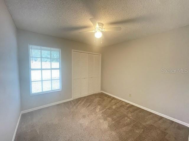 unfurnished bedroom featuring ceiling fan, a textured ceiling, a closet, and dark colored carpet