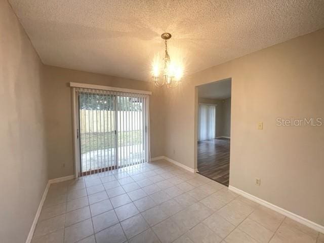 tiled spare room with a chandelier and a textured ceiling