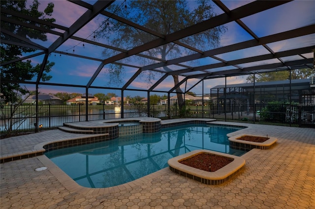 pool at dusk with a patio area, an in ground hot tub, glass enclosure, and a water view