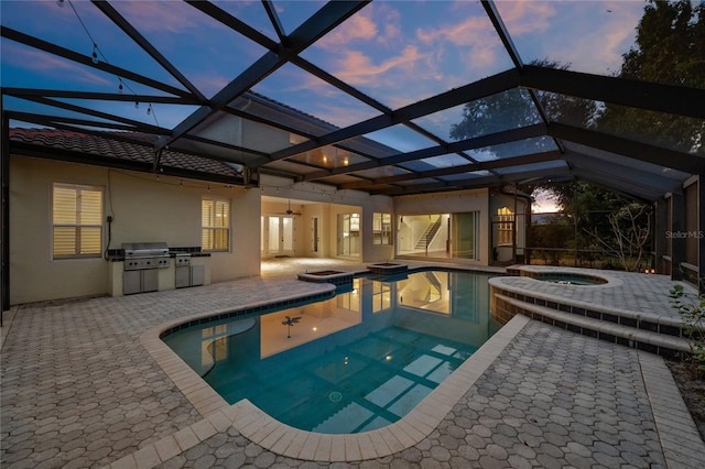 pool at dusk featuring a lanai, an in ground hot tub, a grill, a patio area, and exterior kitchen