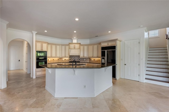 kitchen with premium range hood, a kitchen breakfast bar, black appliances, an island with sink, and dark stone counters