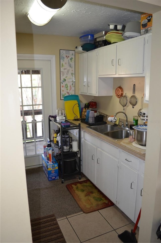 kitchen with light tile patterned floors, sink, a textured ceiling, and white cabinets