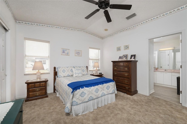 bedroom with ensuite bathroom, lofted ceiling, light colored carpet, ceiling fan, and a textured ceiling