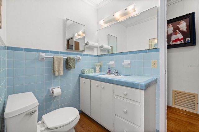 bathroom with toilet, crown molding, wood-type flooring, tile walls, and vanity