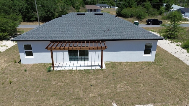 rear view of property featuring a shingled roof, a pergola, stucco siding, and a yard