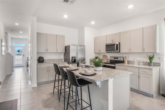 kitchen featuring sink, a breakfast bar area, stainless steel appliances, light stone countertops, and a kitchen island with sink