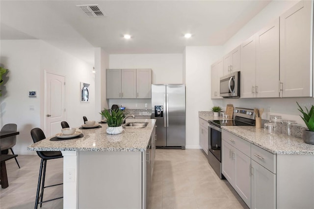 kitchen with stainless steel appliances, light stone countertops, a center island with sink, and a kitchen bar