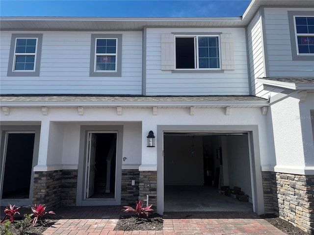 view of exterior entry with a garage, stone siding, and decorative driveway