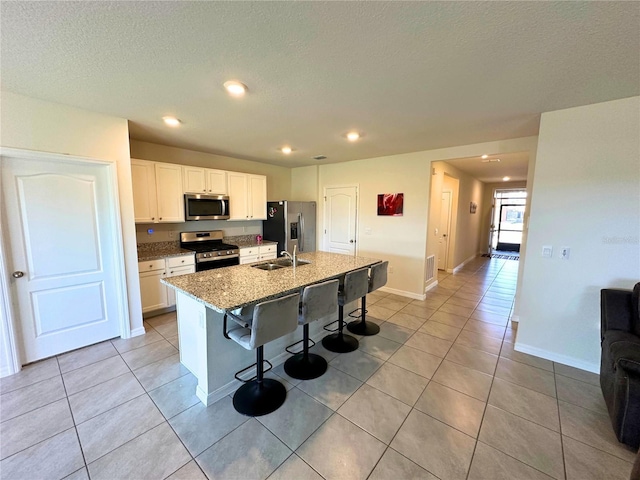 kitchen with a breakfast bar area, white cabinetry, appliances with stainless steel finishes, dark stone counters, and a kitchen island with sink