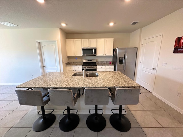 kitchen featuring appliances with stainless steel finishes, white cabinetry, an island with sink, a kitchen breakfast bar, and light stone countertops