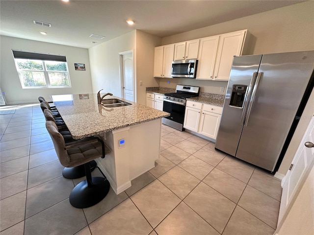 kitchen with sink, appliances with stainless steel finishes, a kitchen island with sink, white cabinetry, and a kitchen bar