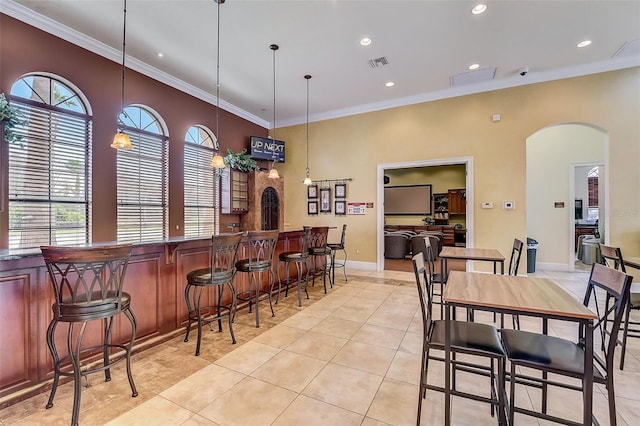 dining space with indoor bar, ornamental molding, and light tile patterned floors