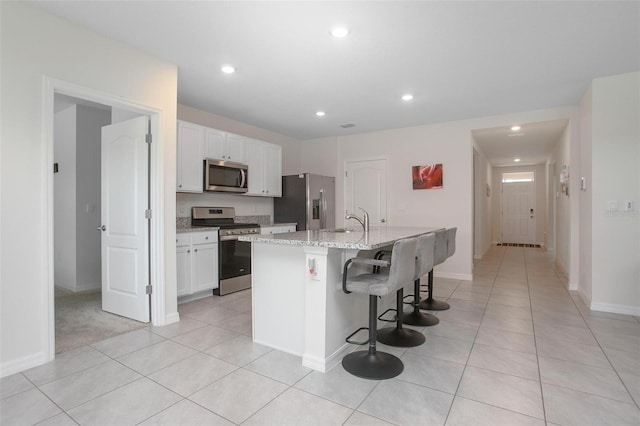 kitchen with a kitchen breakfast bar, appliances with stainless steel finishes, a kitchen island with sink, and white cabinets