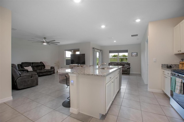 kitchen featuring a sink, white cabinetry, open floor plan, light stone countertops, and a center island with sink