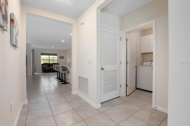 corridor with washer / dryer, visible vents, baseboards, and light tile patterned floors