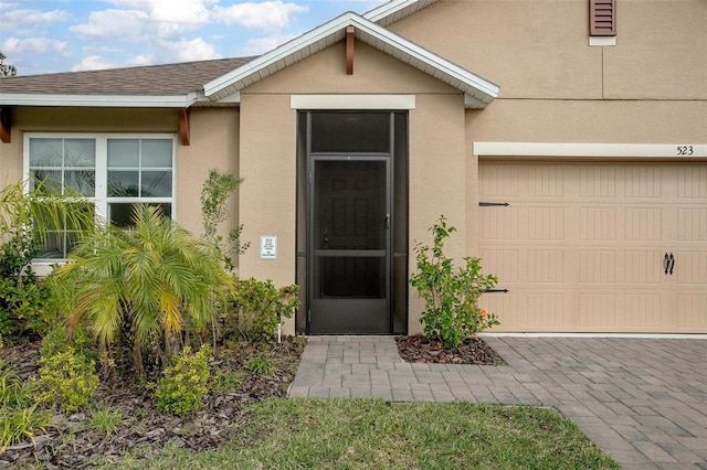 entrance to property featuring a garage, a shingled roof, and stucco siding