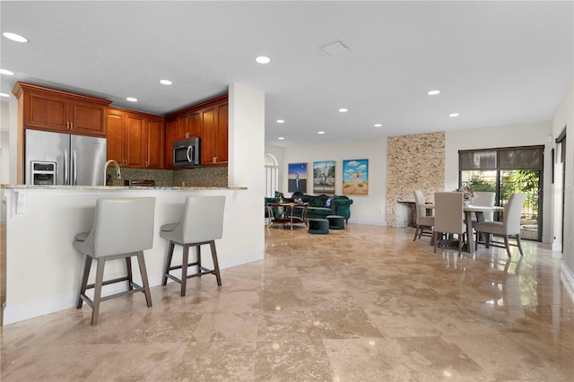 kitchen featuring a breakfast bar area, stainless steel appliances, light stone counters, tasteful backsplash, and kitchen peninsula