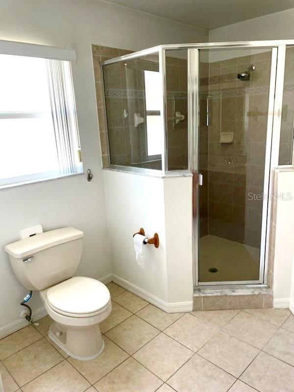 bathroom with tile patterned floors, toilet, and a shower with door