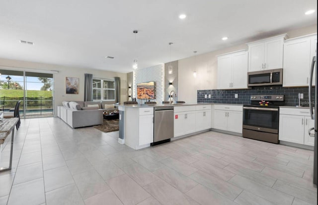 kitchen featuring hanging light fixtures, appliances with stainless steel finishes, white cabinets, and kitchen peninsula