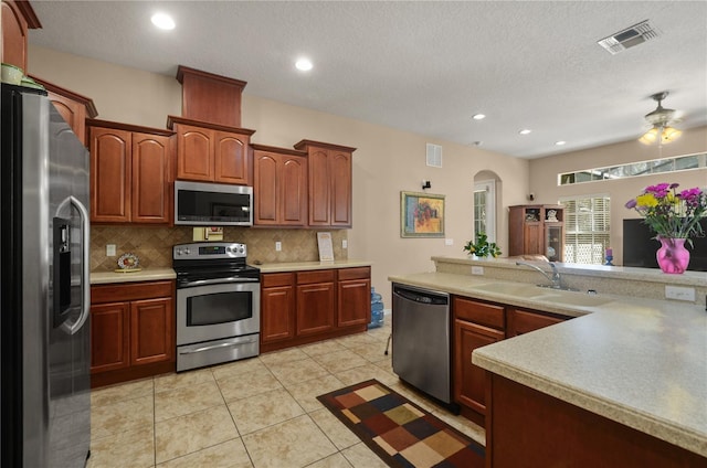 kitchen with sink, backsplash, light tile patterned floors, stainless steel appliances, and a textured ceiling