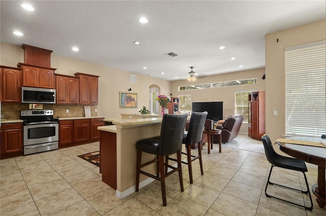 kitchen featuring tasteful backsplash, a breakfast bar area, a center island, light tile patterned floors, and stainless steel appliances