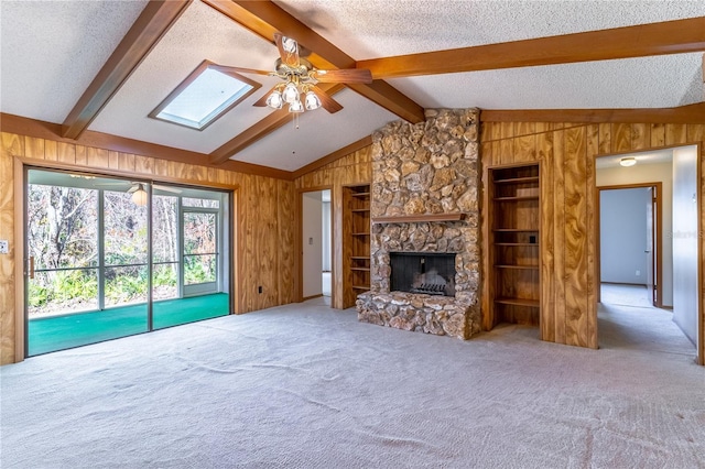 carpeted living room with ceiling fan, vaulted ceiling with skylight, a textured ceiling, and wood walls