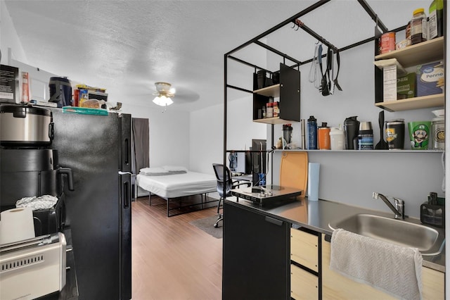 interior space featuring black refrigerator, wood-type flooring, sink, ceiling fan, and a textured ceiling