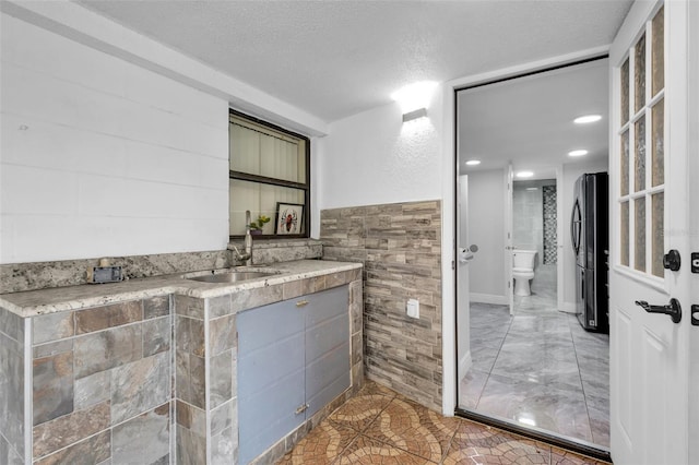 bathroom featuring tile walls, sink, toilet, and a textured ceiling