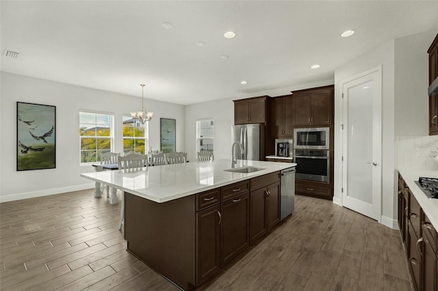 kitchen with sink, a breakfast bar area, decorative light fixtures, appliances with stainless steel finishes, and a kitchen island with sink