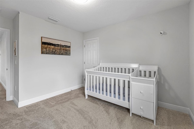 carpeted bedroom featuring a crib and a textured ceiling