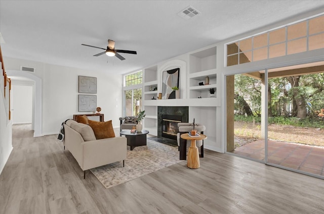 living room featuring ceiling fan, built in features, a fireplace, and light hardwood / wood-style flooring