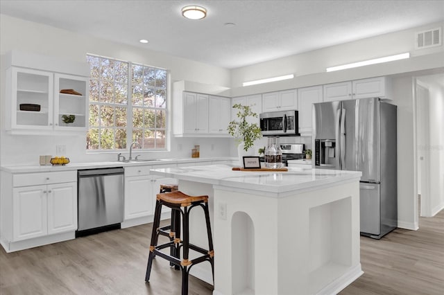 kitchen with a breakfast bar, stainless steel appliances, light stone countertops, white cabinets, and a kitchen island