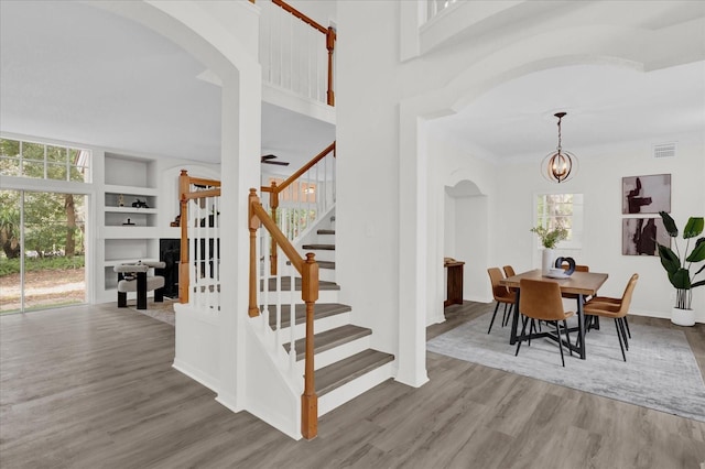 staircase with an inviting chandelier, hardwood / wood-style flooring, plenty of natural light, and a high ceiling