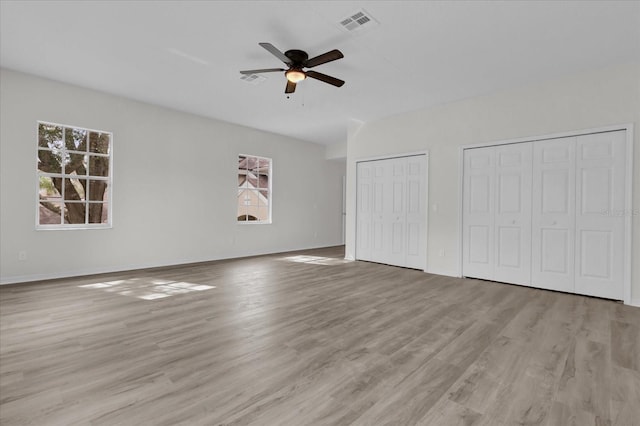 unfurnished bedroom with multiple closets, ceiling fan, and light wood-type flooring