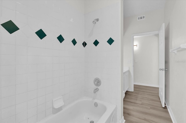 bathroom with hardwood / wood-style flooring, tiled shower / bath, and vanity