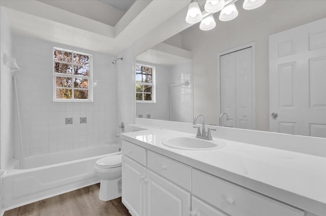 full bathroom with wood-type flooring, tiled shower / bath, vanity, and toilet