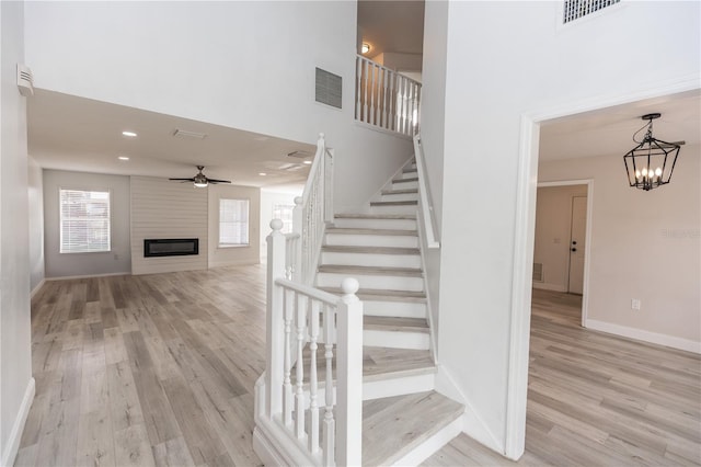 staircase featuring hardwood / wood-style flooring, a high ceiling, ceiling fan with notable chandelier, and a fireplace