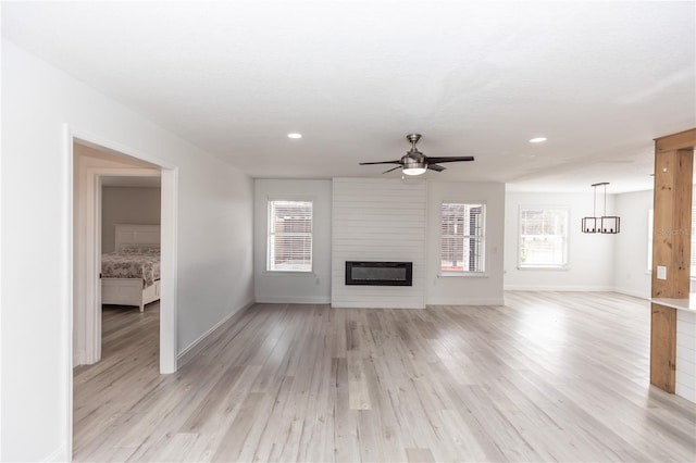 unfurnished living room featuring ceiling fan with notable chandelier, light hardwood / wood-style floors, and a large fireplace