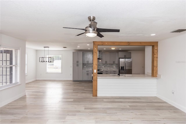 interior space featuring gray cabinetry, backsplash, stainless steel appliances, kitchen peninsula, and light wood-type flooring