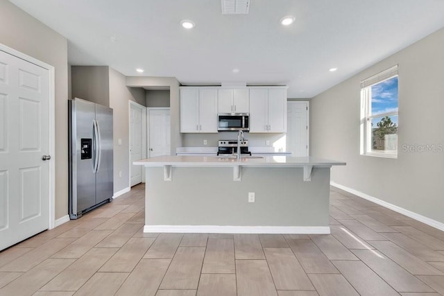 kitchen with appliances with stainless steel finishes, a breakfast bar, white cabinetry, sink, and a kitchen island with sink