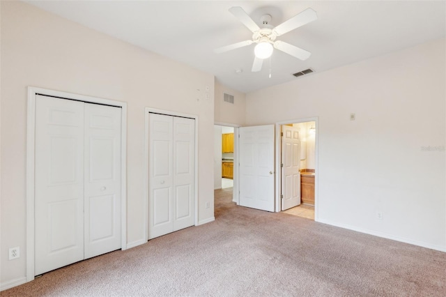 unfurnished bedroom featuring multiple closets, light colored carpet, ceiling fan, and ensuite bath