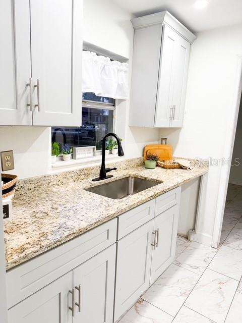 kitchen featuring sink, white cabinets, and light stone counters