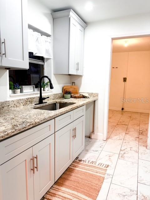 kitchen with white cabinetry, sink, a fireplace, and light stone countertops