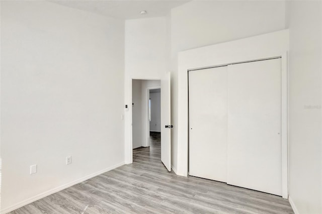 unfurnished bedroom featuring a high ceiling, light hardwood / wood-style floors, and a closet