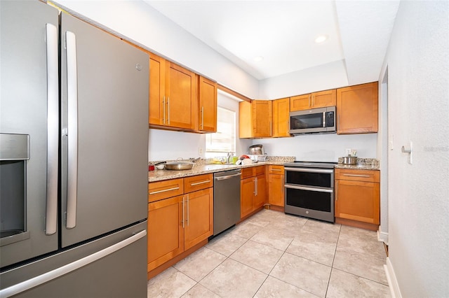 kitchen with light tile patterned floors, light stone countertops, sink, and appliances with stainless steel finishes