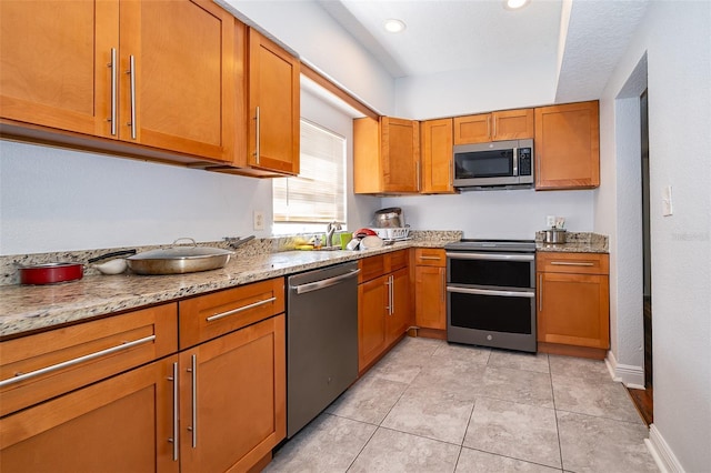 kitchen featuring stainless steel appliances, light stone countertops, sink, and light tile patterned floors