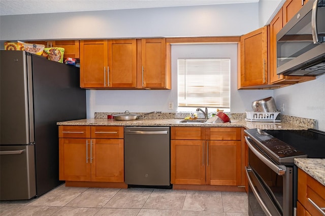 kitchen with stainless steel appliances, light tile patterned flooring, light stone countertops, and sink