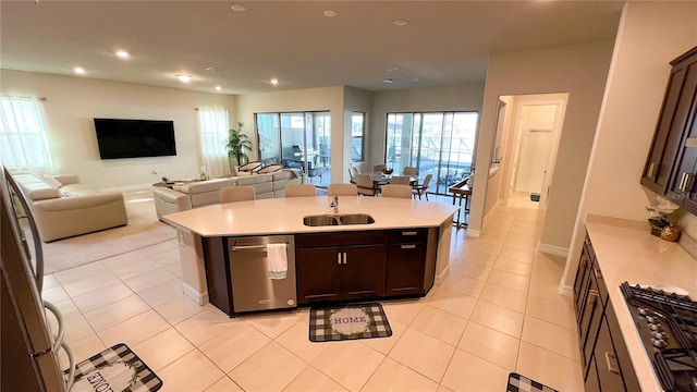 kitchen featuring sink, light tile patterned floors, stainless steel appliances, dark brown cabinetry, and an island with sink