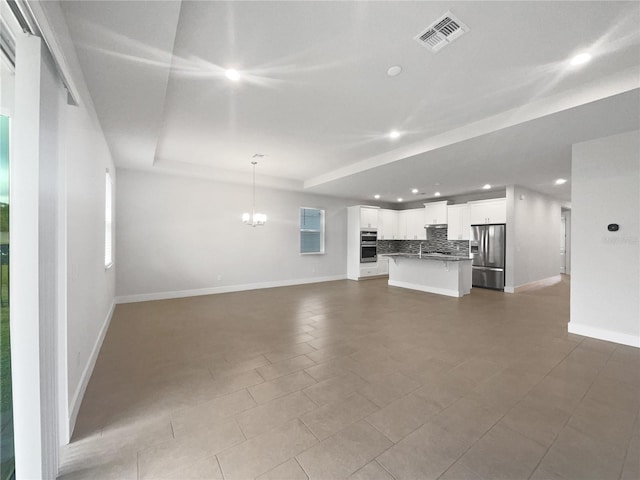 unfurnished living room featuring a raised ceiling and a chandelier